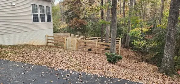 Wood rail fence and gate enclosing a yard on a wooded lot