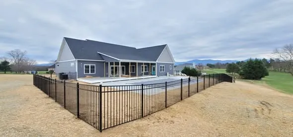 Black ornamental aluminum fence enclosing a pool behind a grey home with mountains beyond