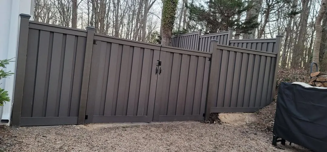 Dark brown composite privacy fence with a double gate beside a house