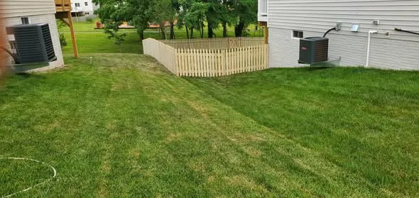 Wood picket fence section installed between two houses on a graded lawn